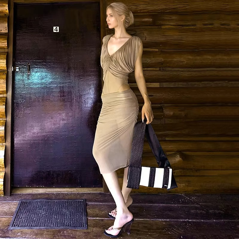 Woman in a beige dress standing in front of a wooden door holding a black and white striped bag.